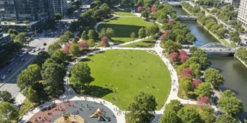 Aerial view of a bustling new urban park with green lawns, paths, trees, and city buildings.