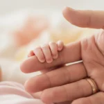 Sure Start Maternity Grant: Your Guide to Claiming £500 Tiny baby hands grasping an adult's finger, representing the Sure Start Maternity Grant support.